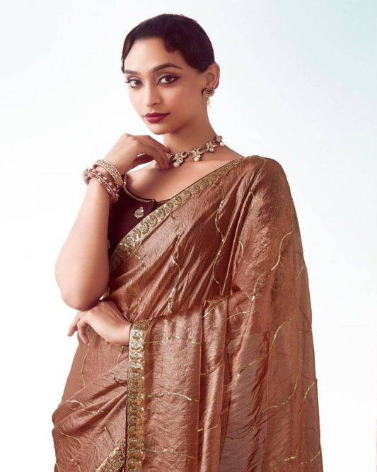 Woman wearing a brown saree with gold details on a white background