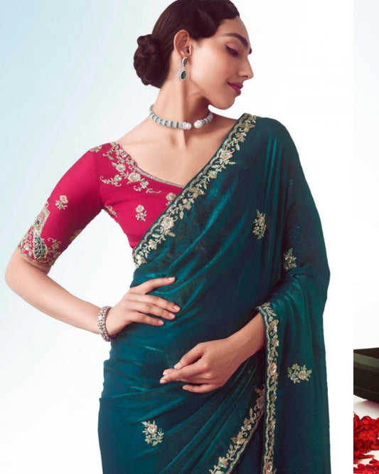 Woman wearing a teal saree with pink blouse, standing against a light blue background.