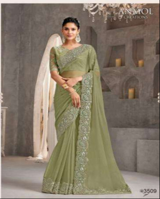 Woman in a green saree with intricate patterns in an elegant indoor setting.