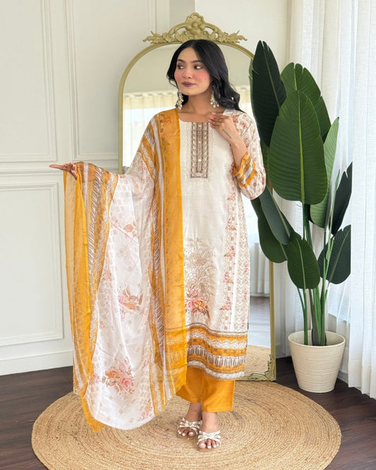 Woman in a white and orange traditional outfit standing in a room with a mirror and plant.