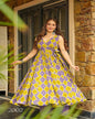Woman in a yellow and purple checkered dress standing in front of a stone wall.