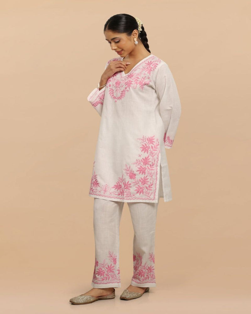 Woman wearing a light-colored kurta with pink floral embroidery on a beige background