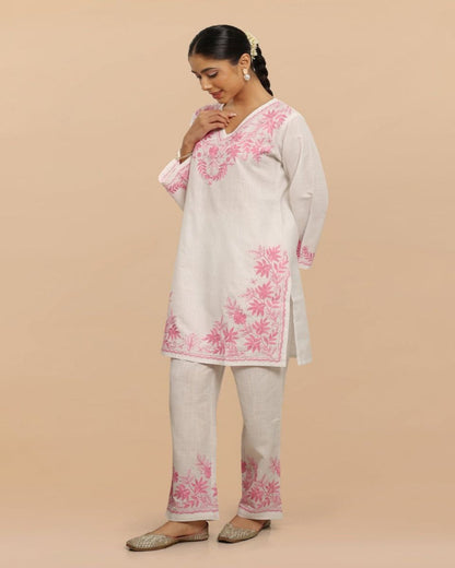 Woman wearing a light-colored kurta with pink floral embroidery on a beige background