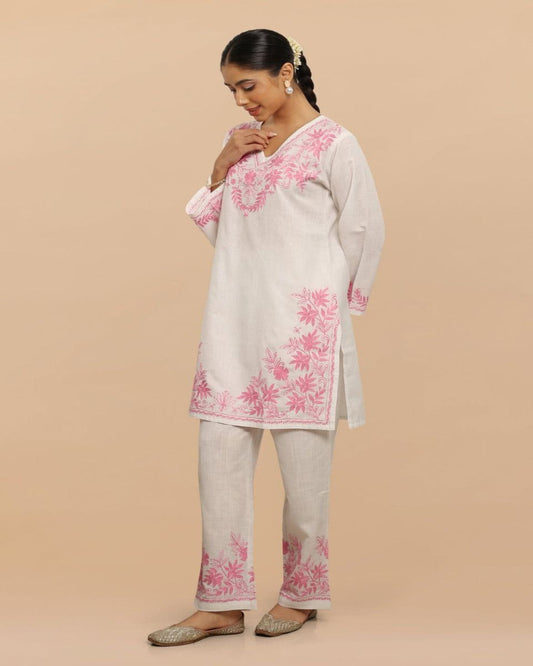 Woman wearing a light-colored kurta with pink floral embroidery on a beige background
