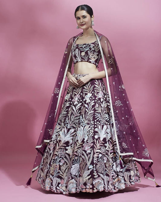 Woman wearing a floral lehenga with a purple dupatta on a pink background