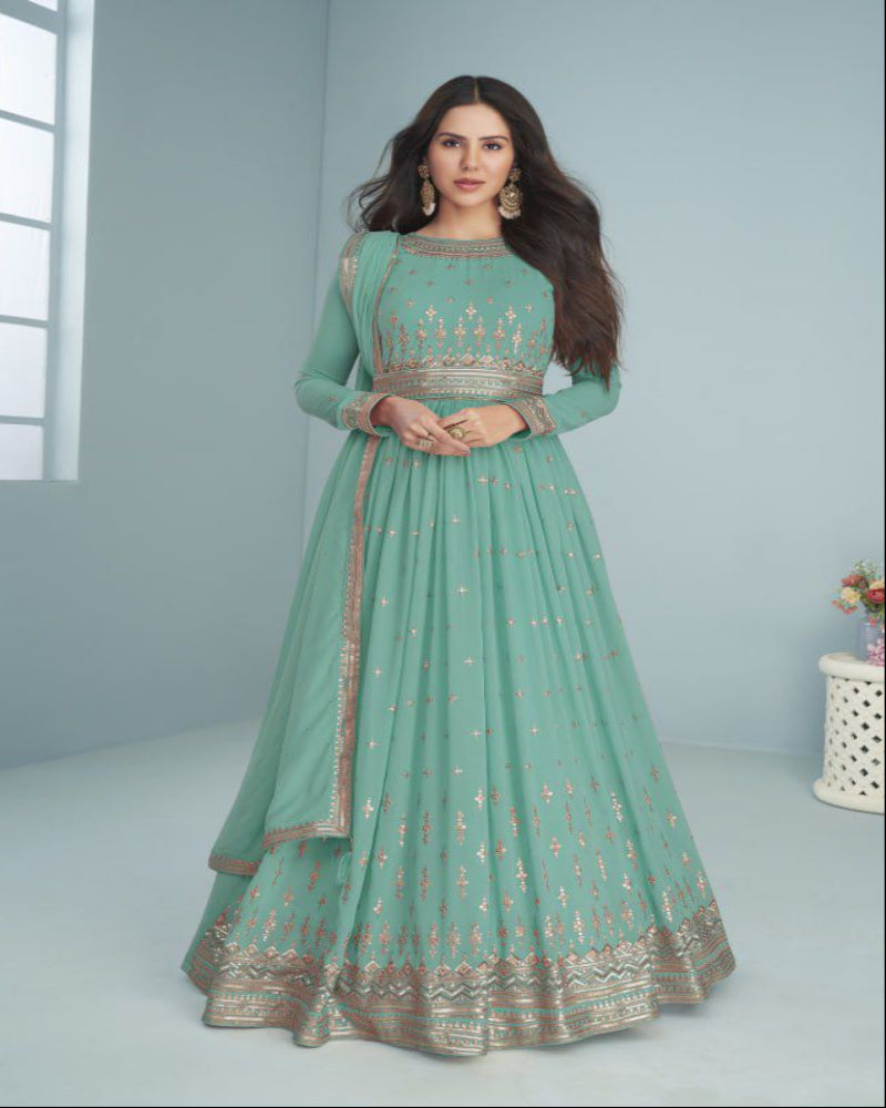 Woman wearing a green traditional outfit with embroidery, standing against a light gray background.