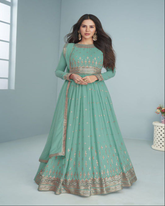 Woman wearing a green traditional outfit with embroidery, standing against a light gray background.