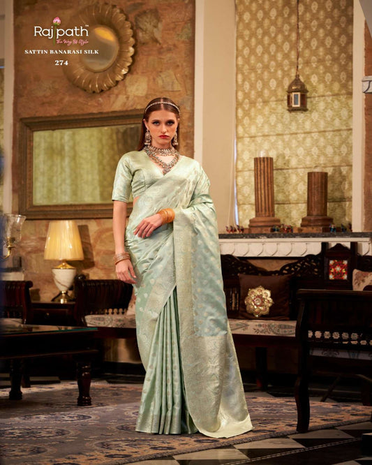 Woman in a light green saree standing in an elegant room with decorative elements.