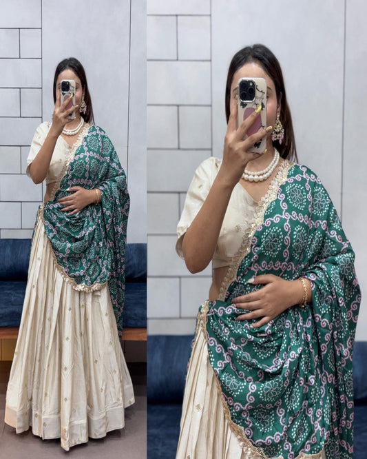 Woman wearing a green and purple patterned dupatta over a cream outfit against a tiled wall.