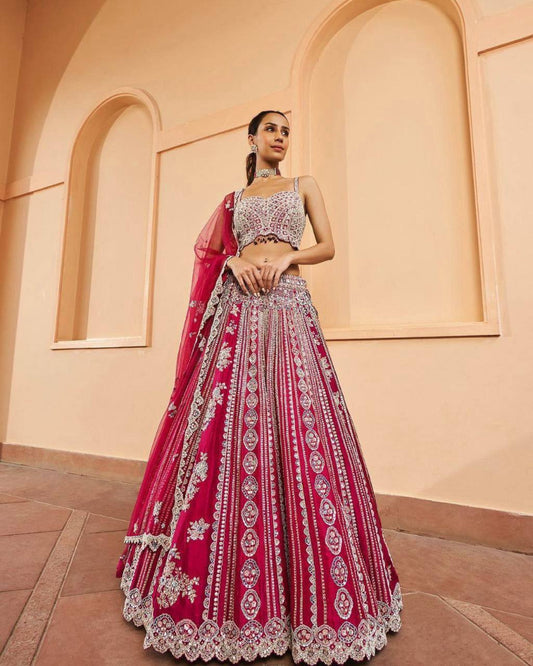 Woman wearing a red and white embroidered traditional outfit with a pink dupatta against a beige wall.