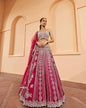 Woman wearing a red and white embroidered traditional outfit with a pink dupatta against a beige wall.
